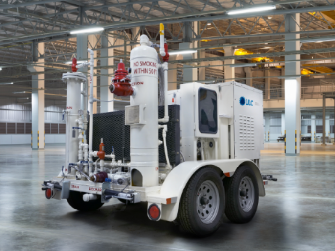 A white trailer is parked in a large empty warehouse.