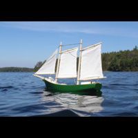 a small green sailboat with white sails is floating on top of a lake .
