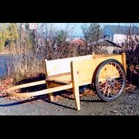 a wooden wheelbarrow is sitting on the side of a road .