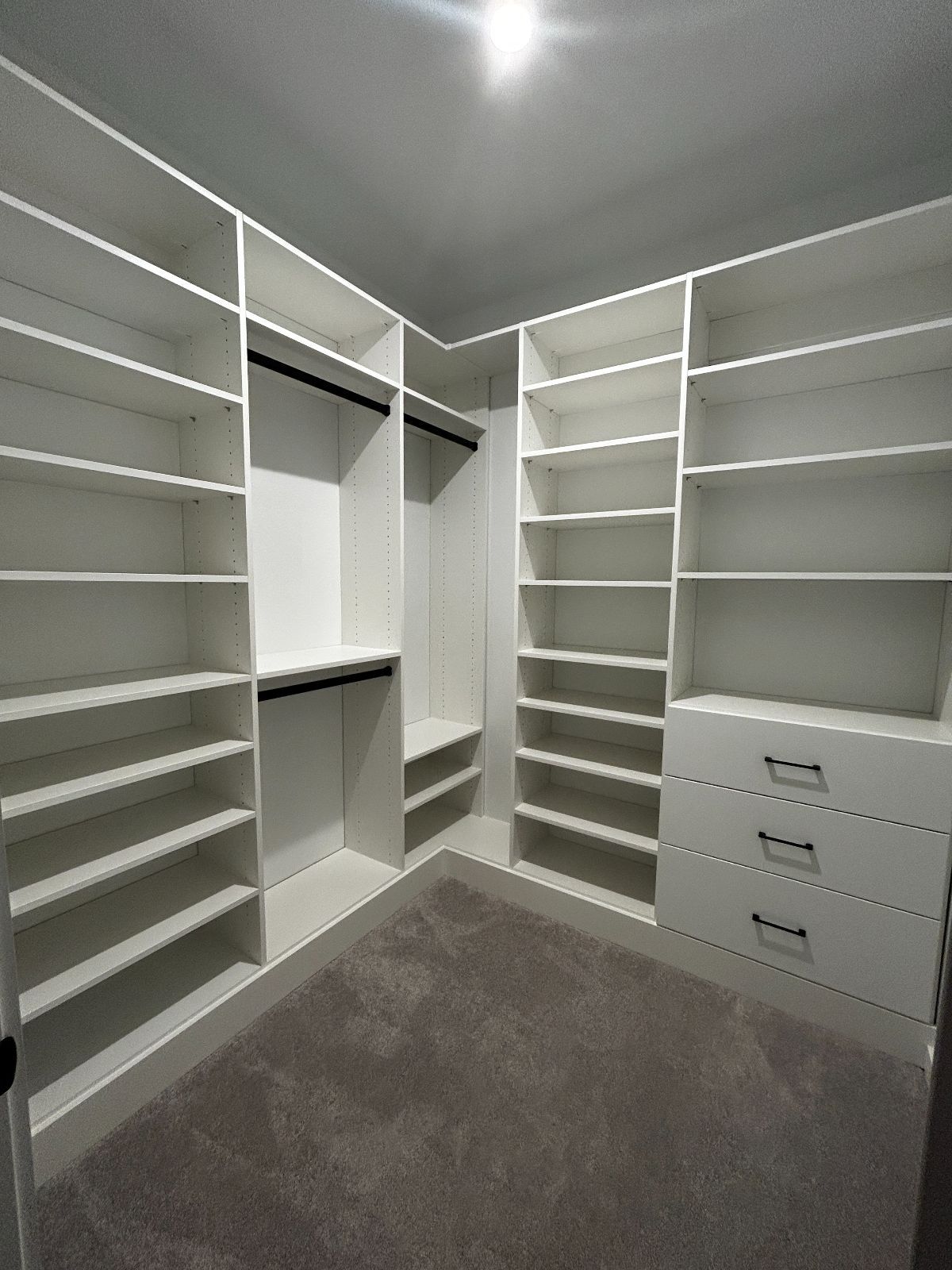 White custom closet with shelves, drawers, and hanging rods. Gray carpet covers the floor.