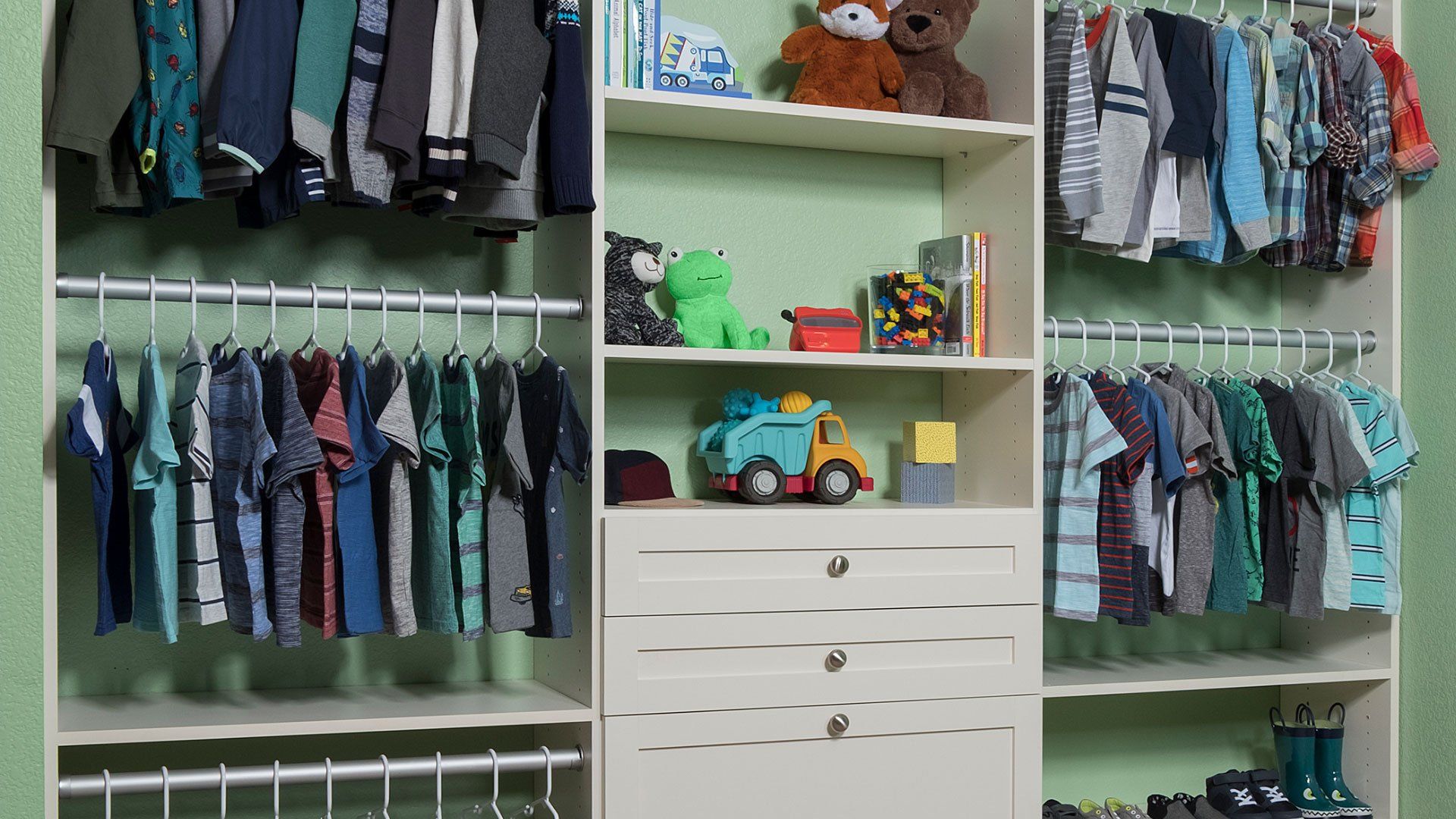 Children’s closet with hanging clothes, shelves, and a white drawer unit with toys and bins