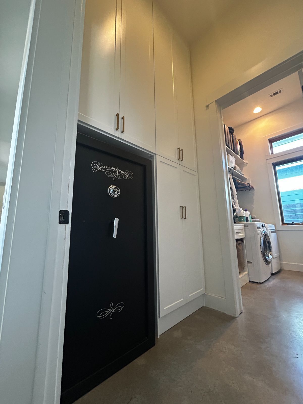 Black safe door built into white cabinets, hallway to a laundry room.