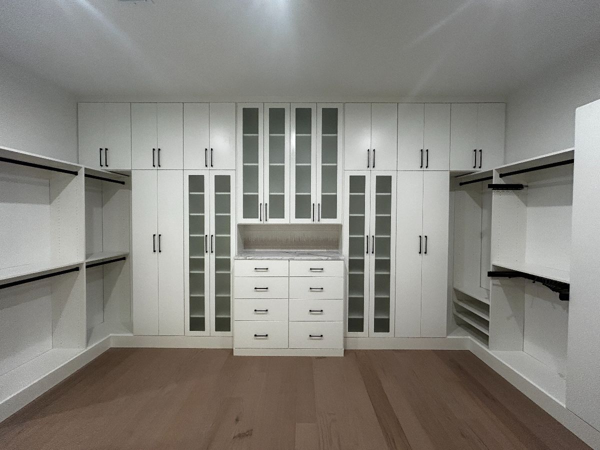 White walk-in closet with built-in cabinetry, drawers, and shelving. Brown flooring.