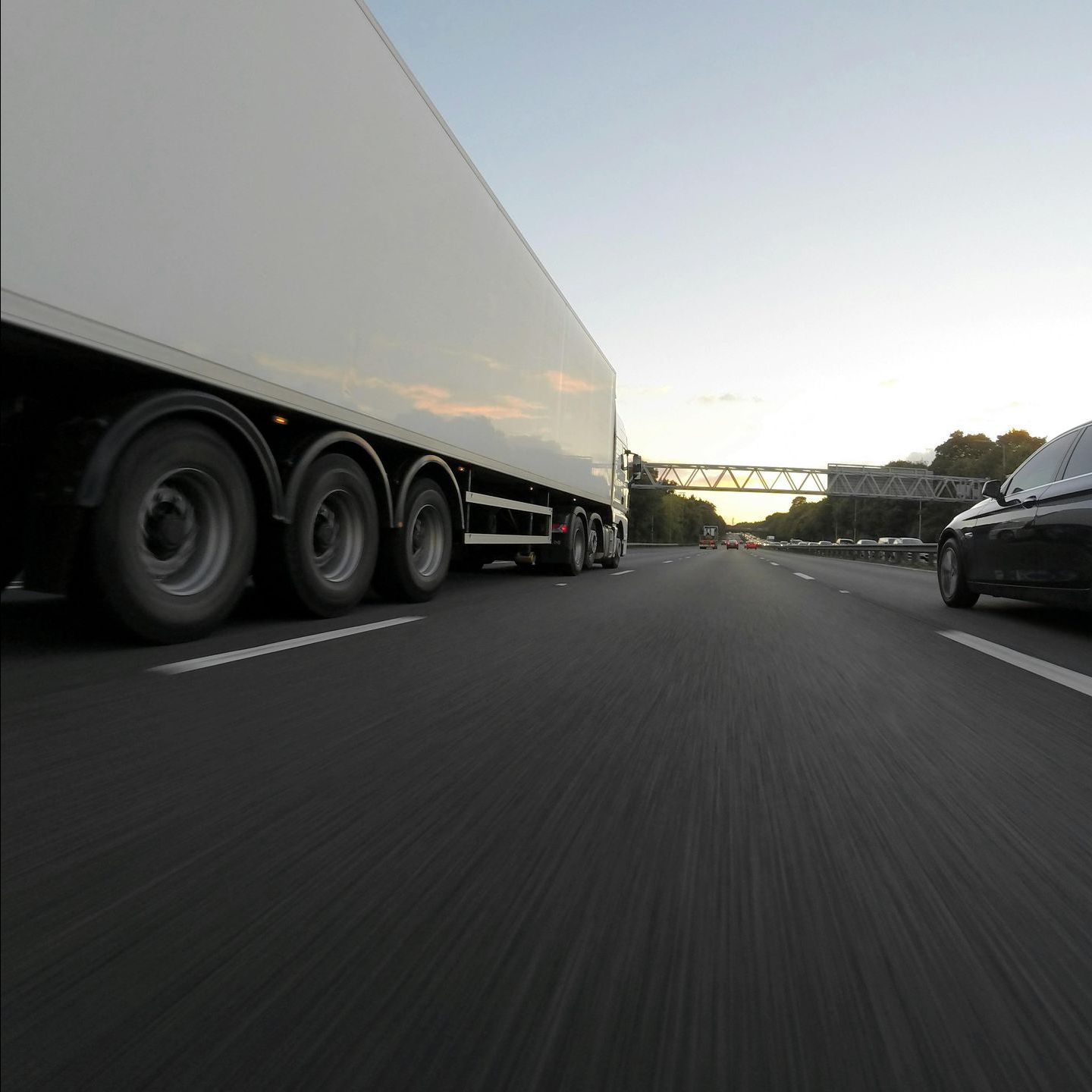 A white truck is driving down a highway next to a black car.