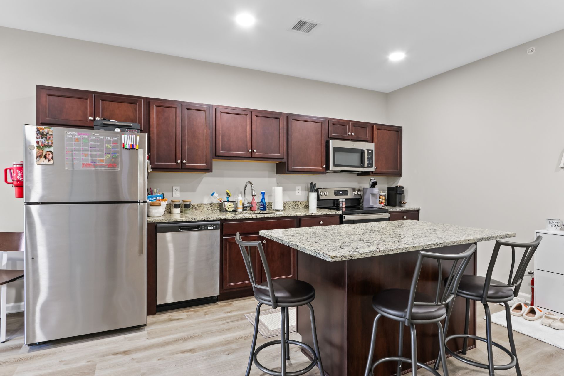 Kitchen with dark wood cabinets, stainless steel appliances, granite island, and bar stools.