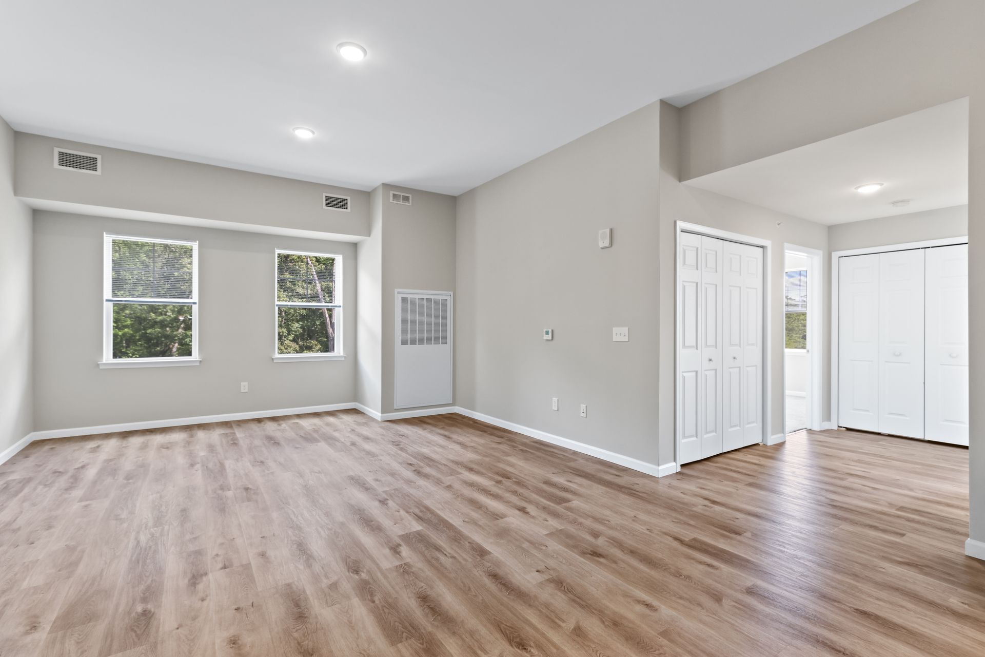 Empty room with light wood floors, gray walls, two windows, and white doors.