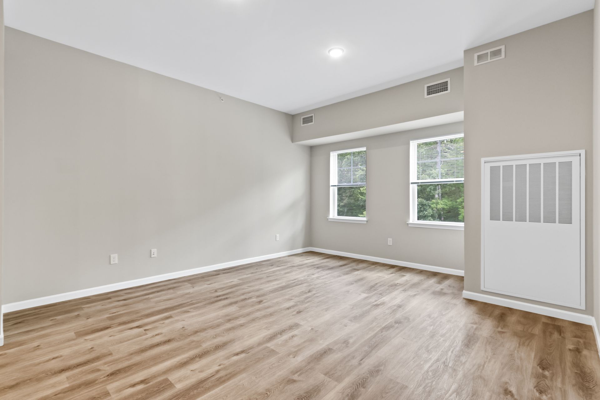 Empty room with wood floors, two windows, and neutral walls.