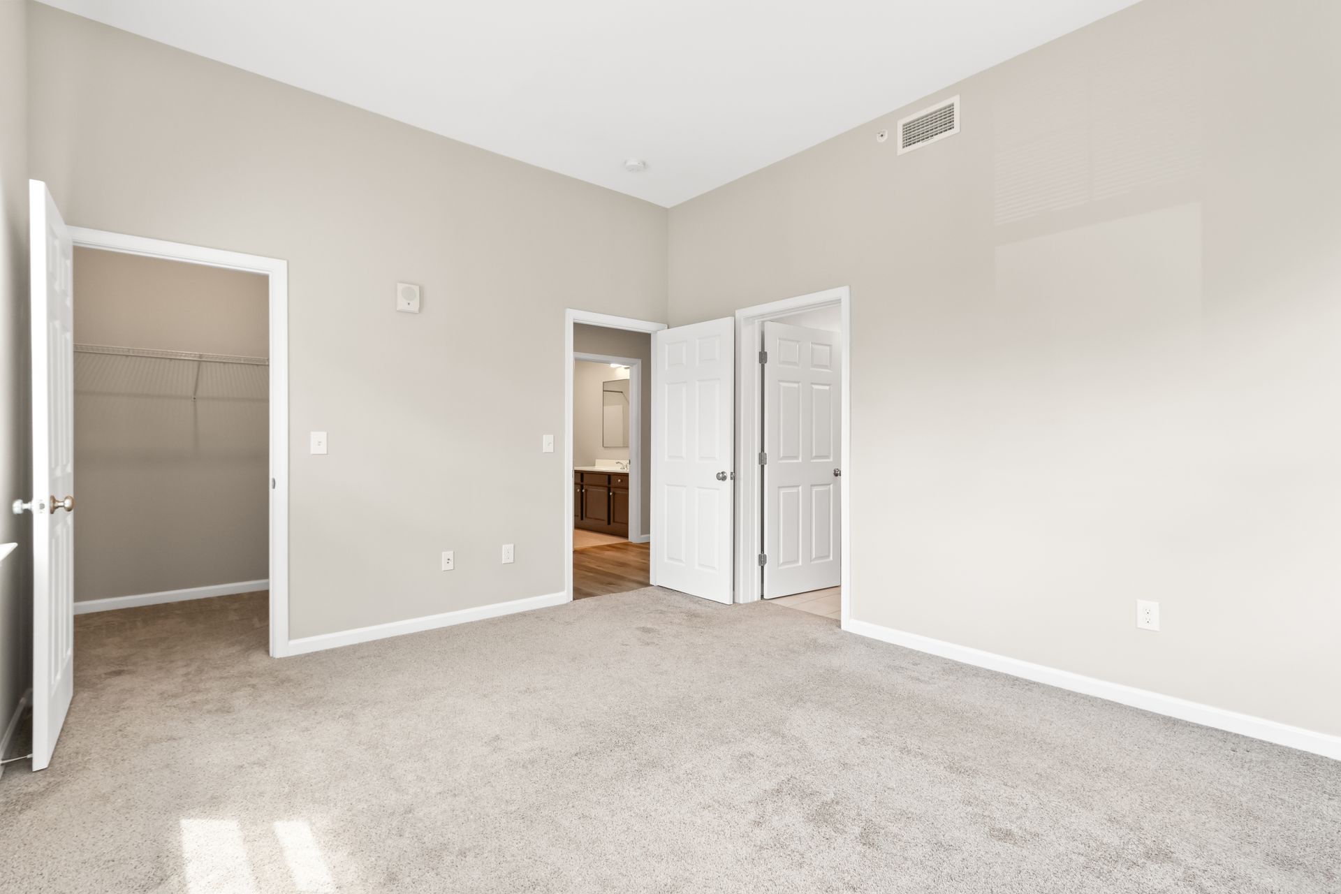 Empty bedroom with carpet, three white doors, and a closet.