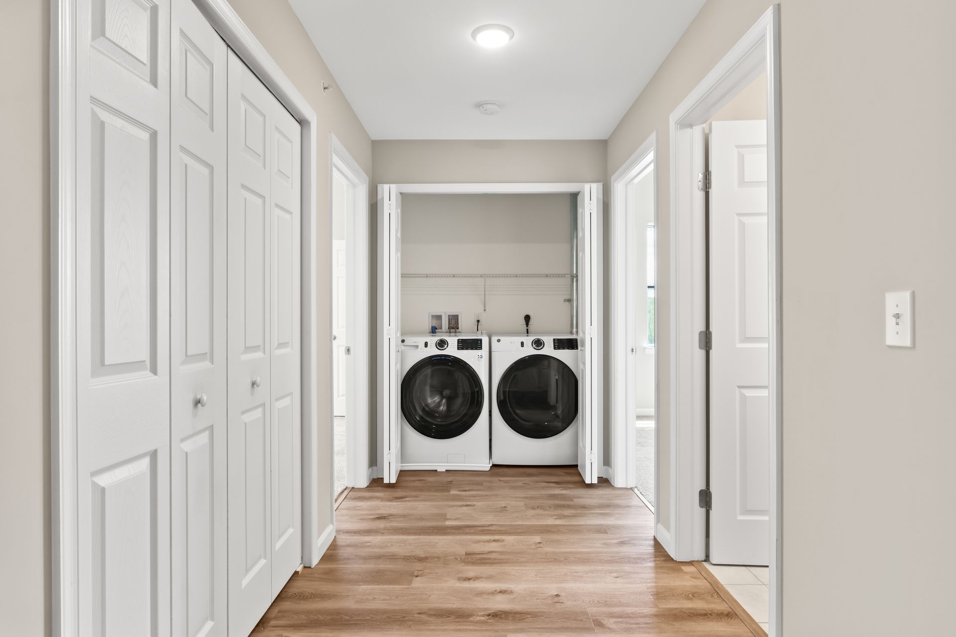 Hallway with white bi-fold doors, washer/dryer, light wood floor, and neutral walls.