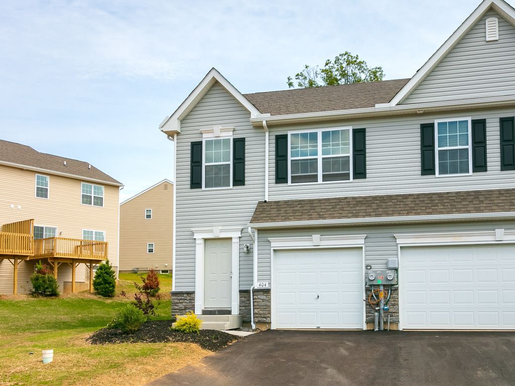 Two-story gray townhome with a white garage door, black shutters, and a lawn in front.
