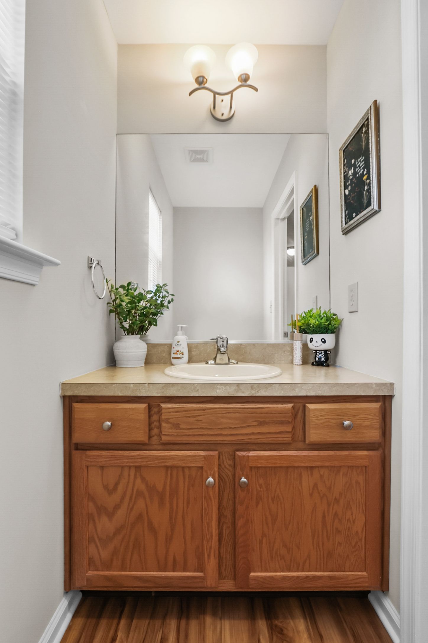 Bathroom vanity with a wood cabinet, beige countertop, mirror, and two small framed artworks.
