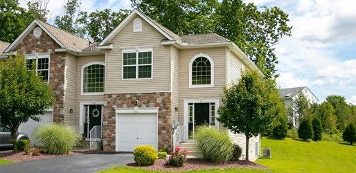 Townhouses with tan siding, stone accents, and manicured landscaping under a blue sky.