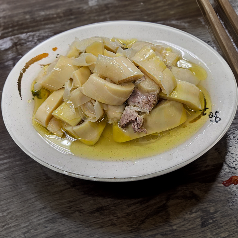 一盤食物，裡面有竹筍和豬肉。白色盤子放在灰色桌上。