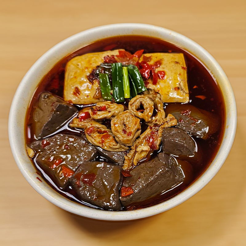 一碗台灣美食，以豆腐、豬血和內臟為特色，浸在紅色的湯汁中，並撒上蔥花。