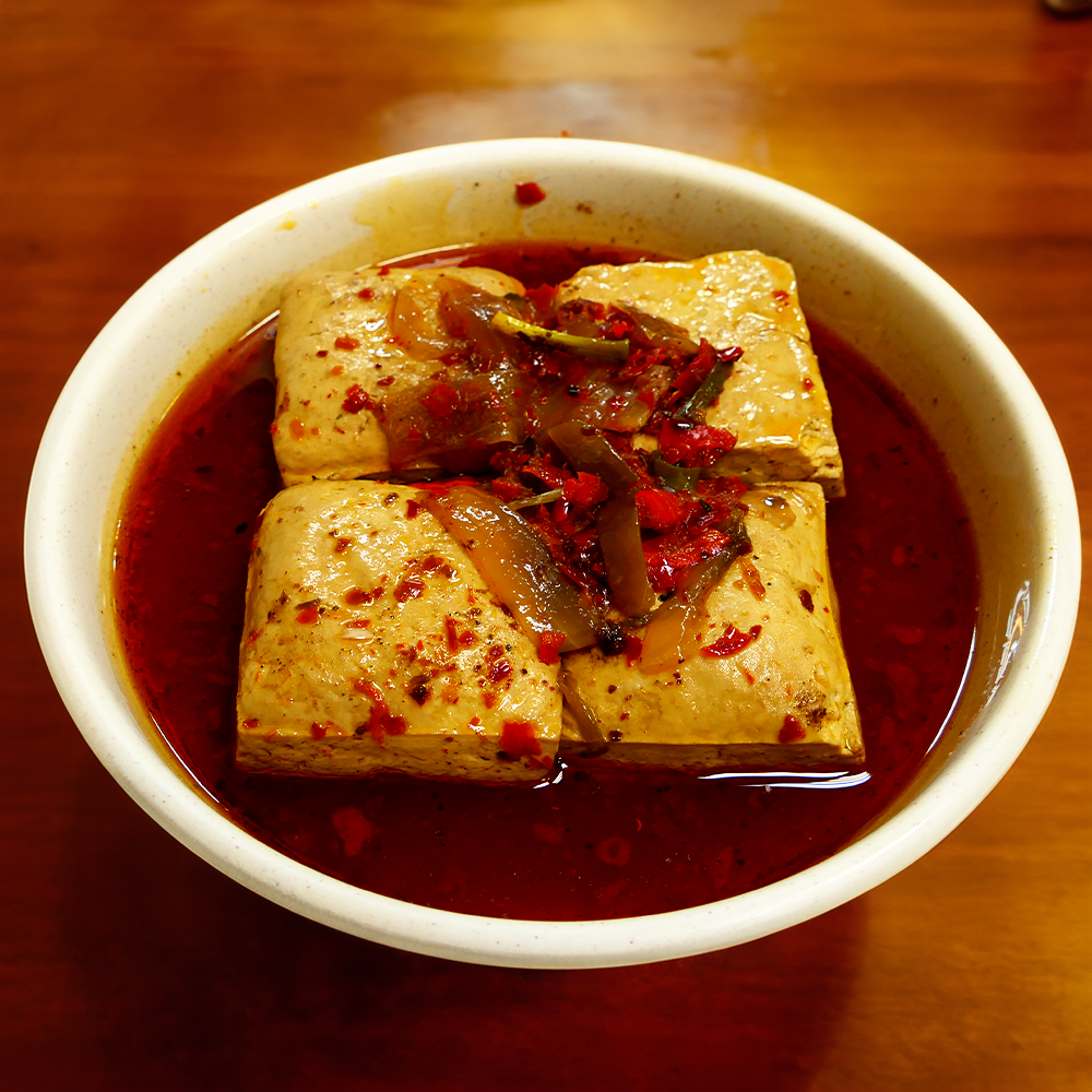 一碗方豆腐，淋上紅辣椒油，撒上洋蔥和辣椒片。