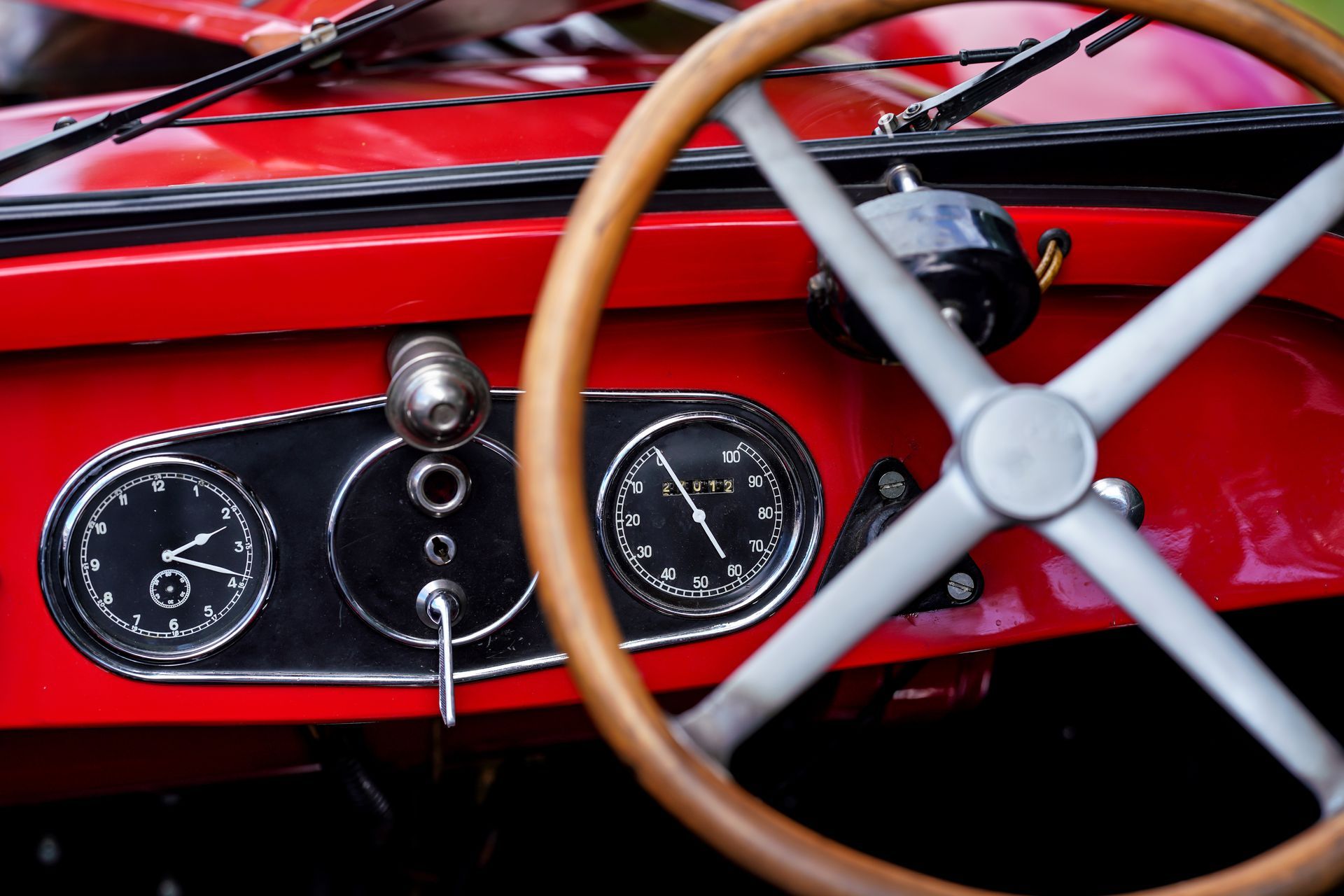Vintage car parts, including chrome gauges and a wooden steering wheel on a red dashboard.