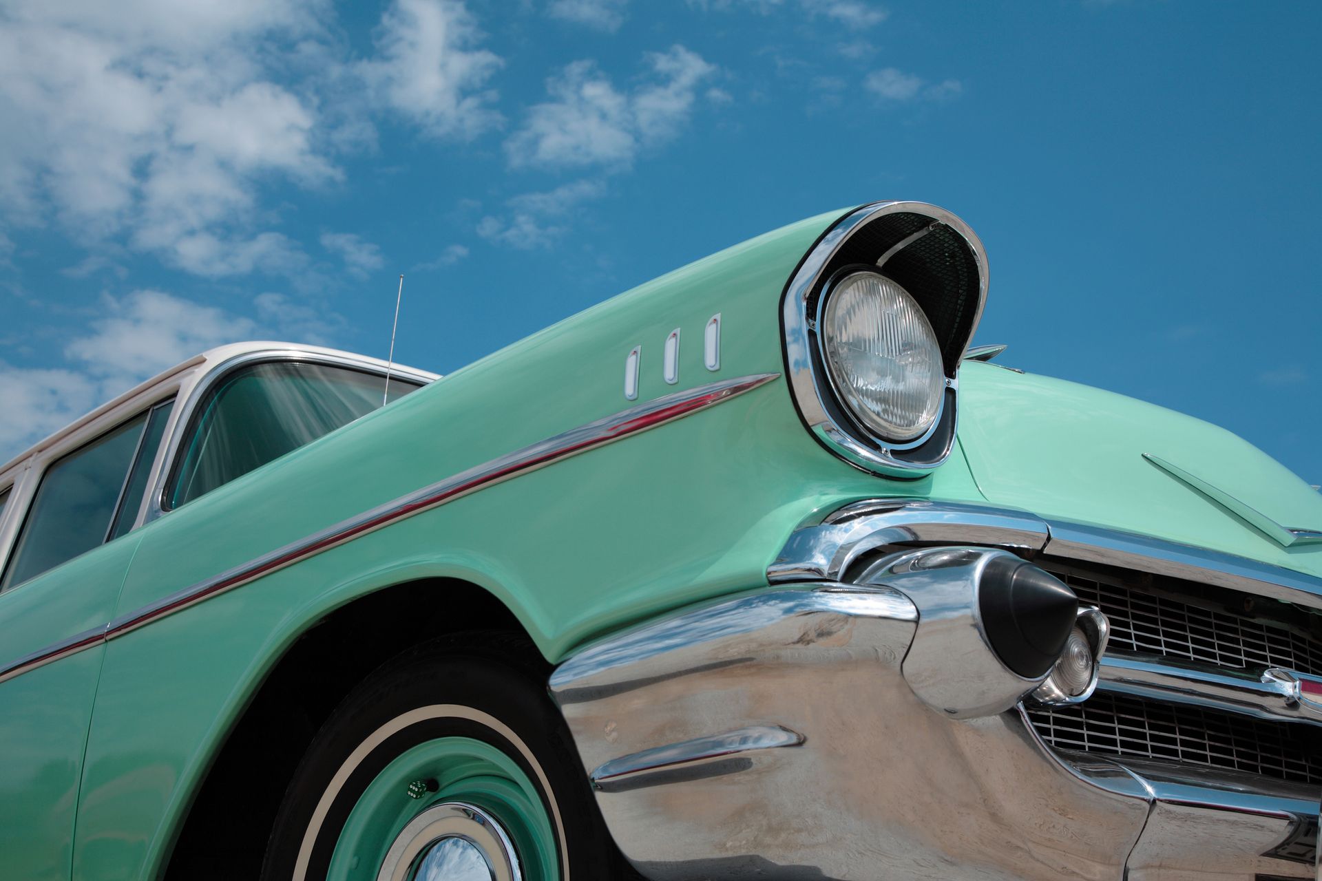 Vintage mint green classic car parked under blue sky with chrome details in bright sunlight presently.
