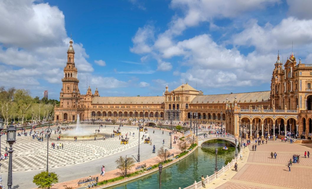 Plaza de España a Siviglia con un canale, una fontana e palazzi in mattoni decorati sotto un cielo azzurro.