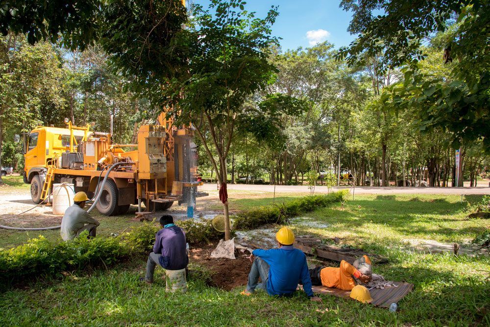 A group of construction workers are sitting in the grass in front of a truck.