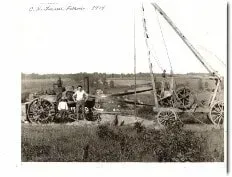 A black and white photo of a group of people standing next to a tractor.