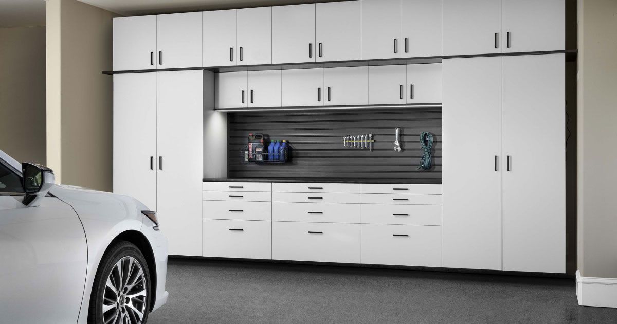 A white car is parked in a garage with white cabinets.