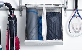 a golf bag , a tennis racket , and a yoga mat are hanging on a rack in a garage .