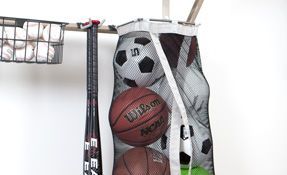 a basketball , soccer ball , and baseball bat are hanging in a mesh bag .