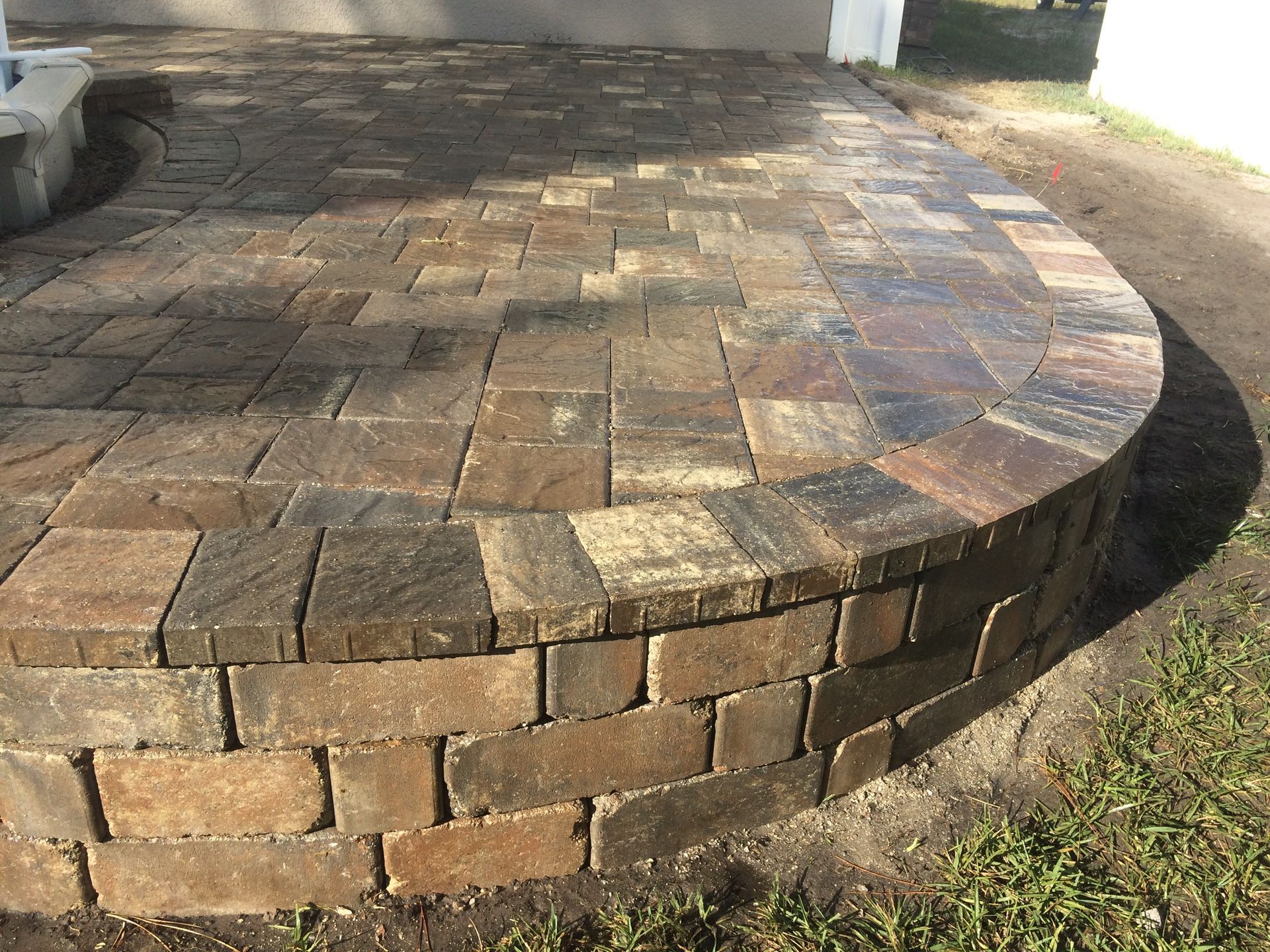 A brick patio is being built in the backyard of a house.
