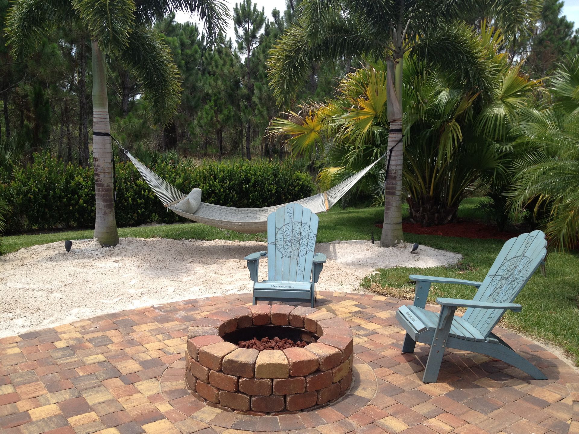 A fire pit with two chairs and a hammock in the background