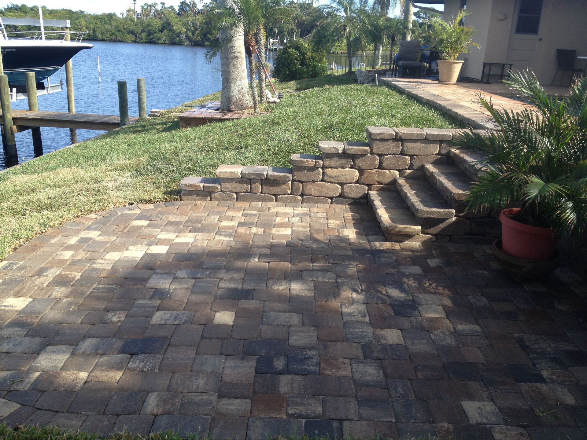 A brick patio with stairs leading up to a dock overlooking a body of water.