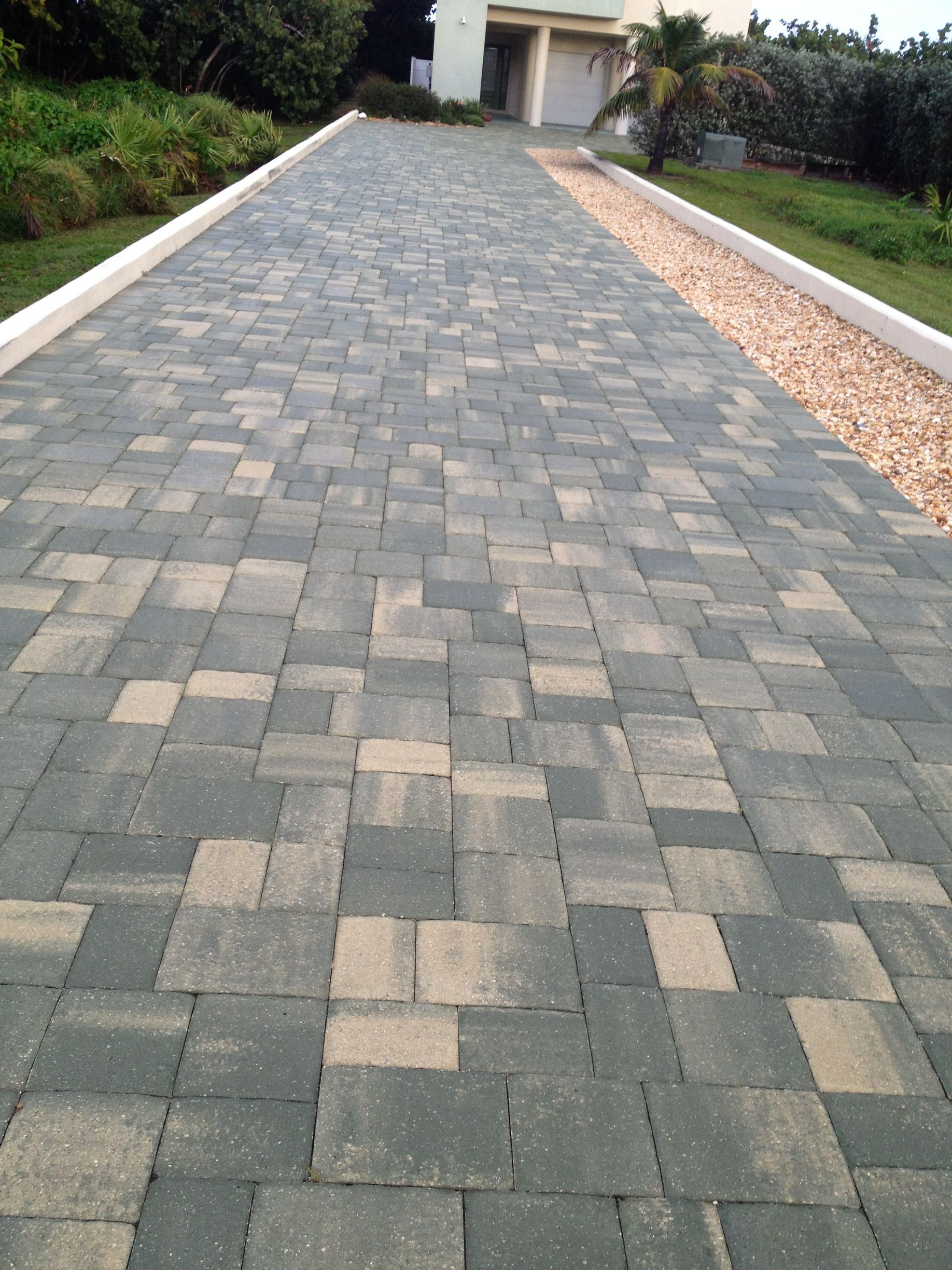 A brick driveway leading to a house with a white curb