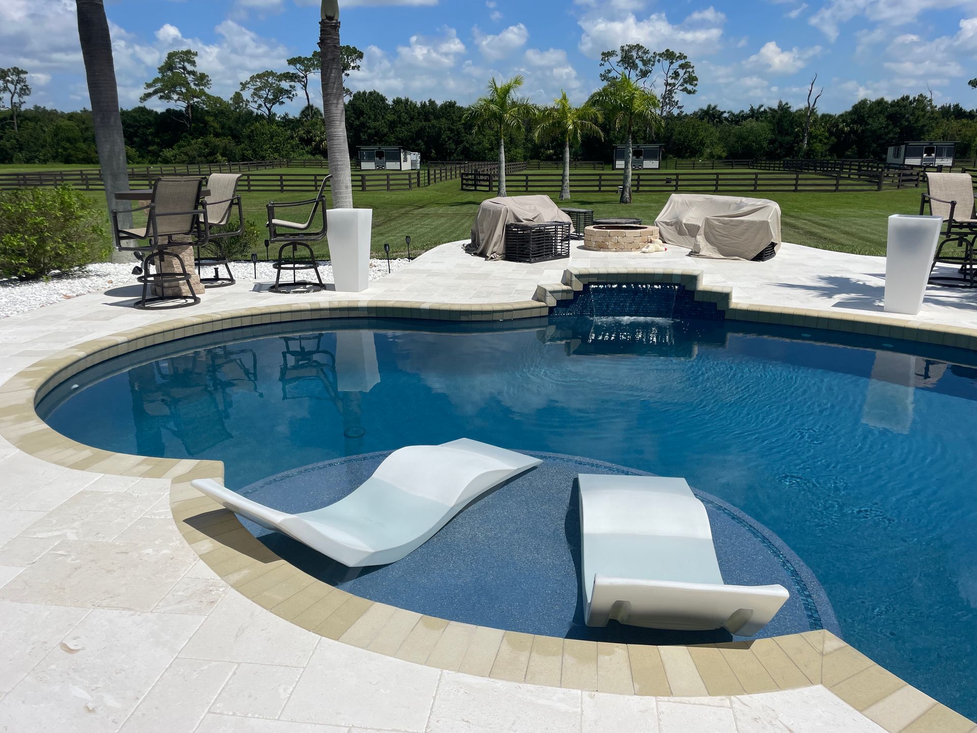 A large swimming pool surrounded by chairs and a fire pit