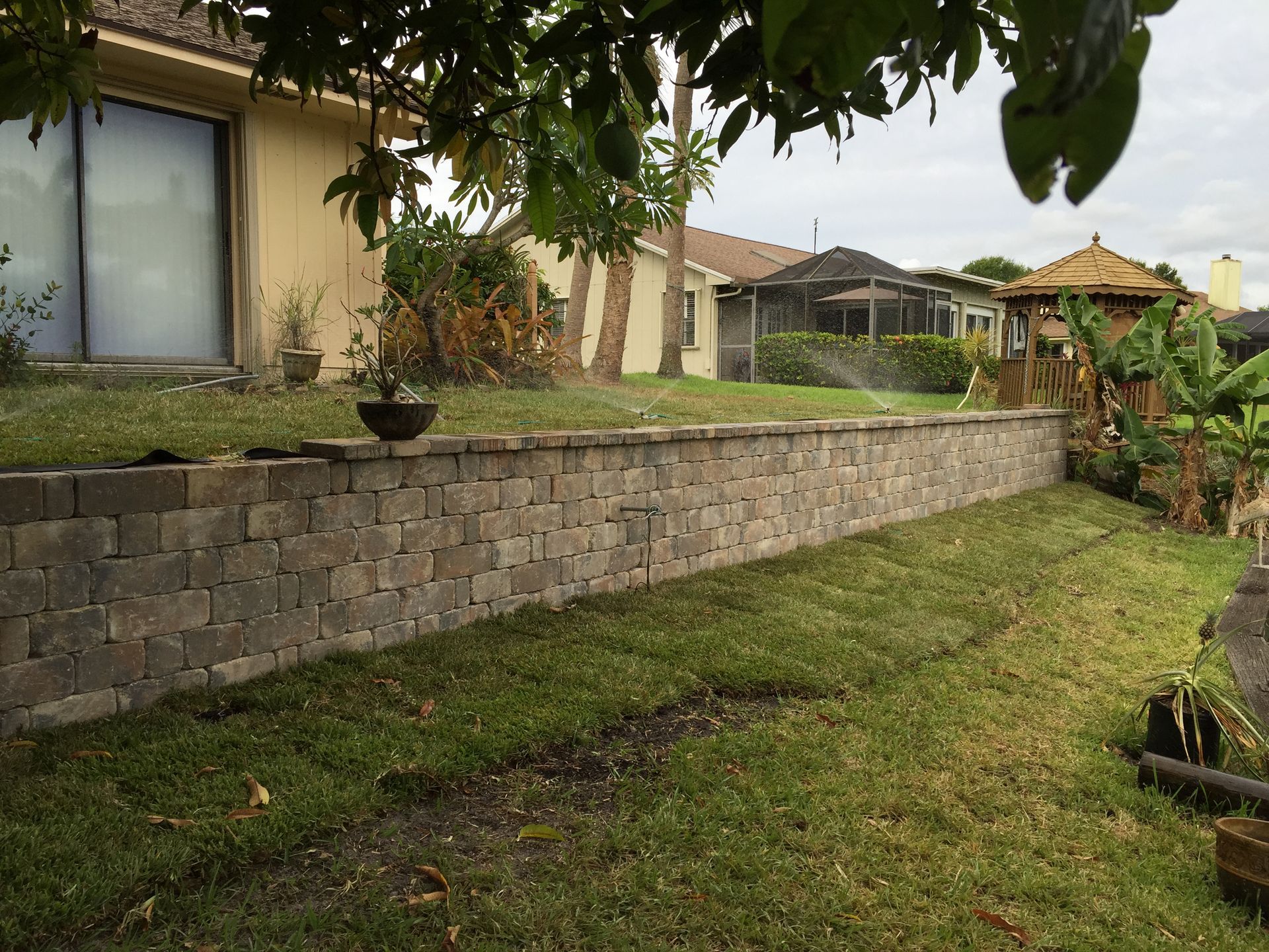 A brick wall surrounds a lush green lawn in front of a house.