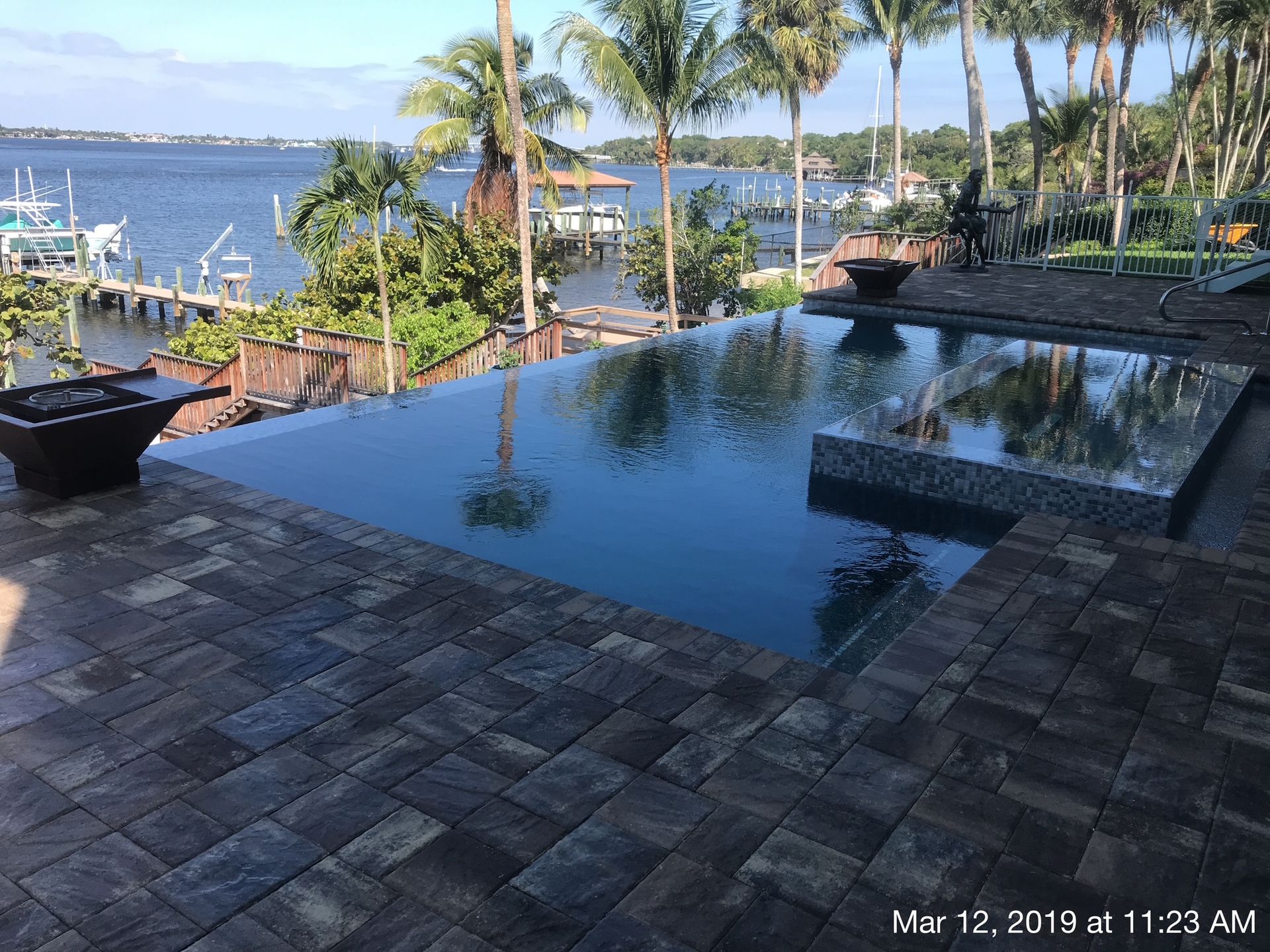 A large swimming pool is surrounded by palm trees and a dock.