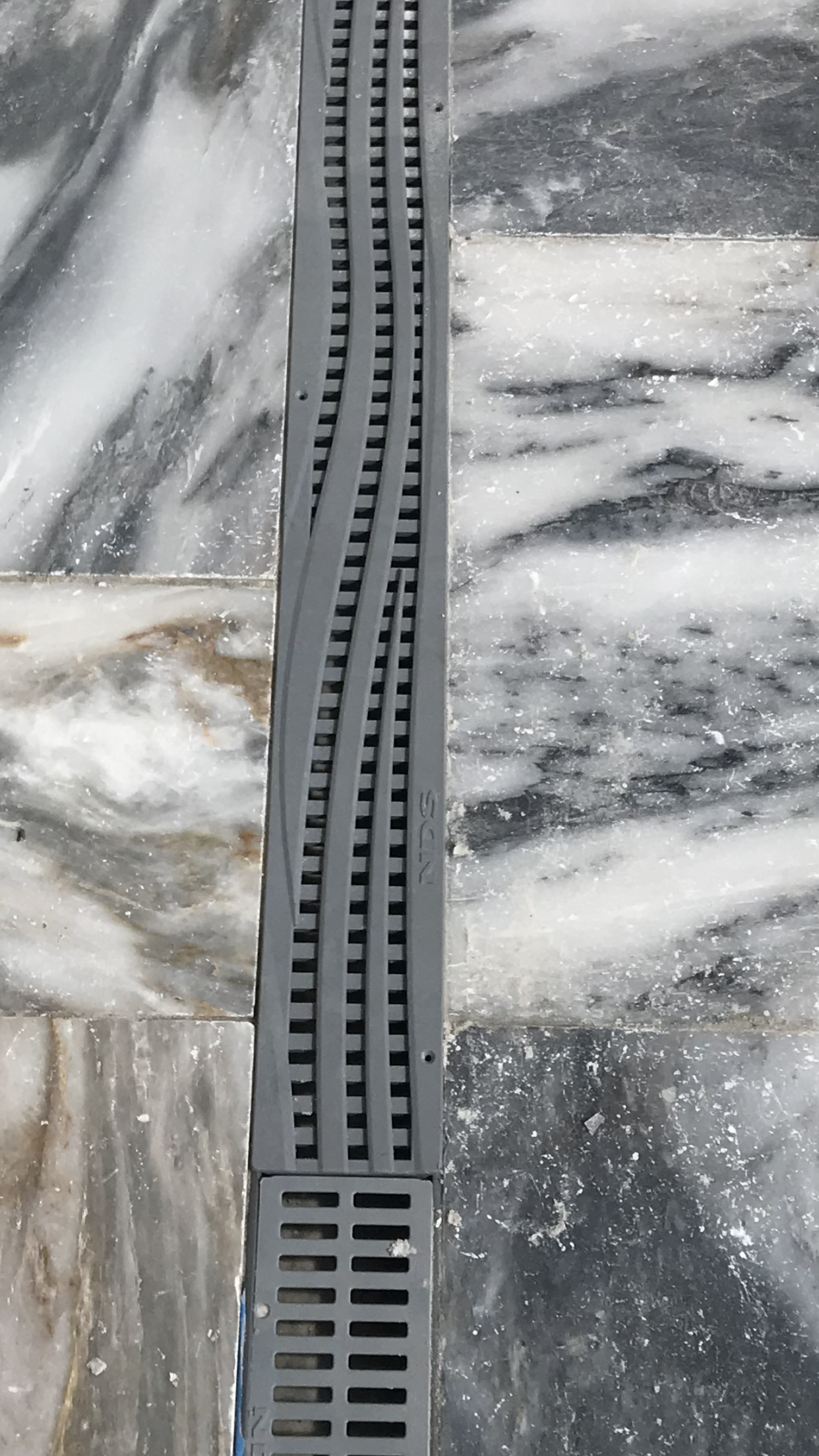 A close up of a drain on a marble floor.
