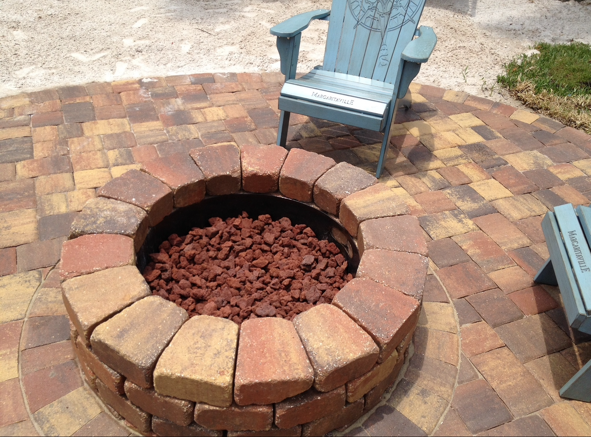 A fire pit made of bricks on a patio with a chair in the background.