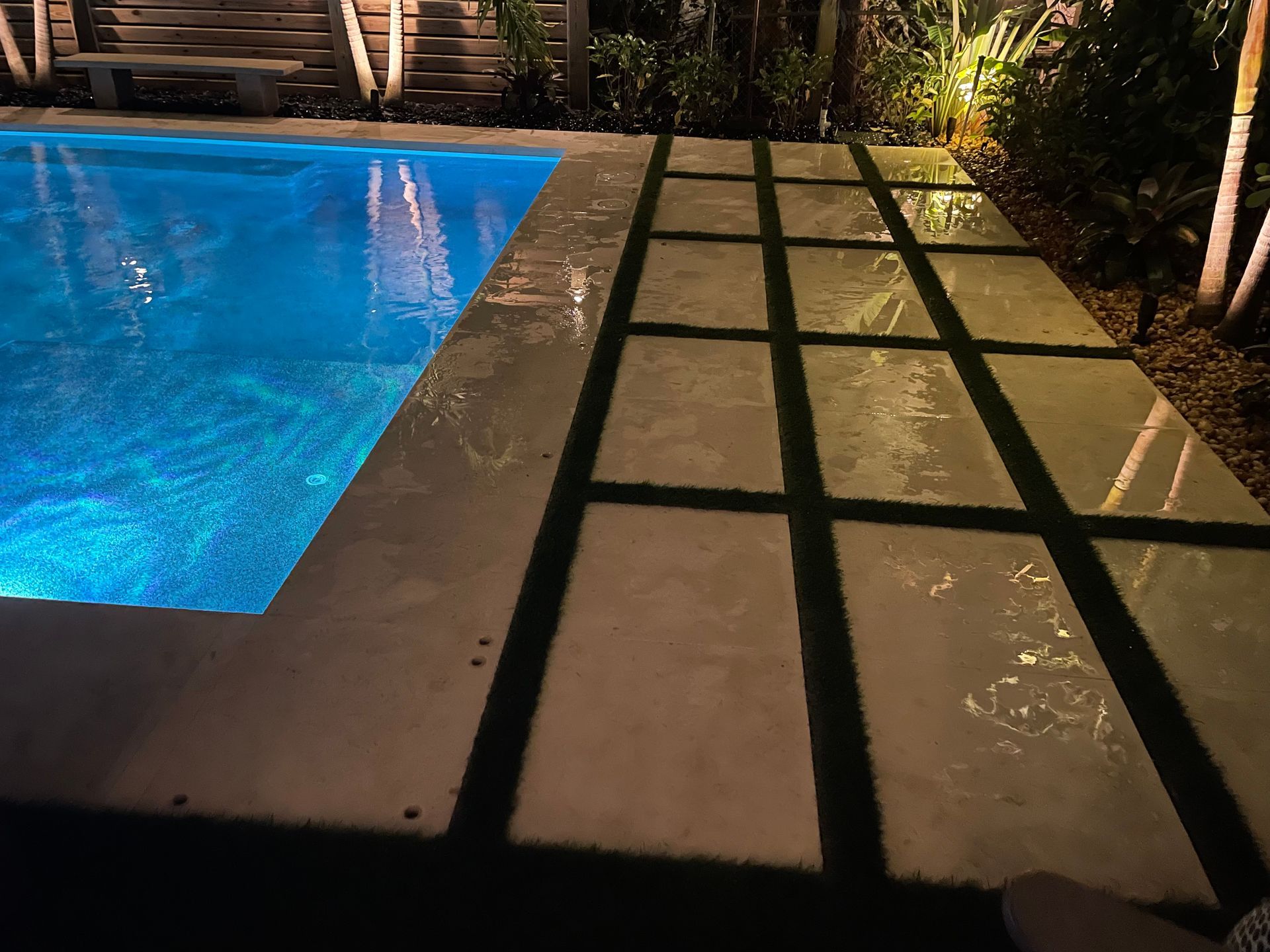 A swimming pool with a walkway leading to it at night