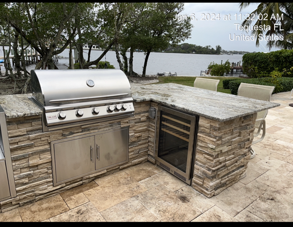 An outdoor kitchen with a grill and a refrigerator