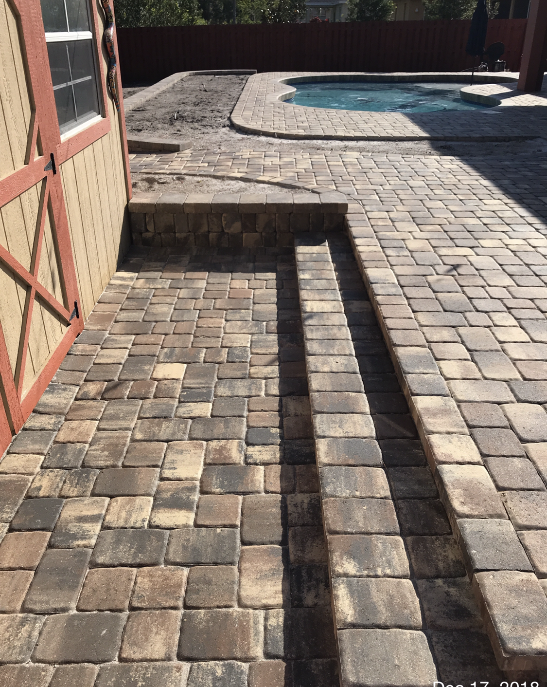 A brick patio with stairs leading to a pool