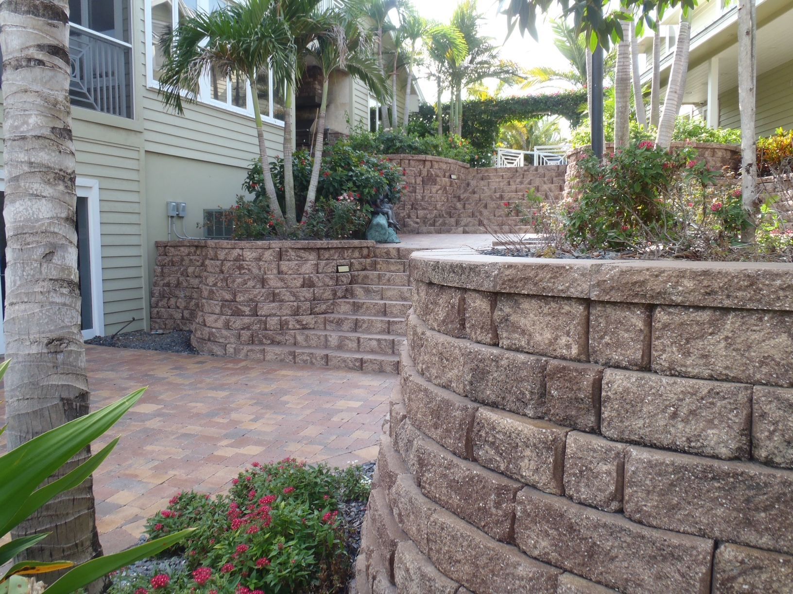 A brick wall is surrounded by flowers and plants in front of a house.