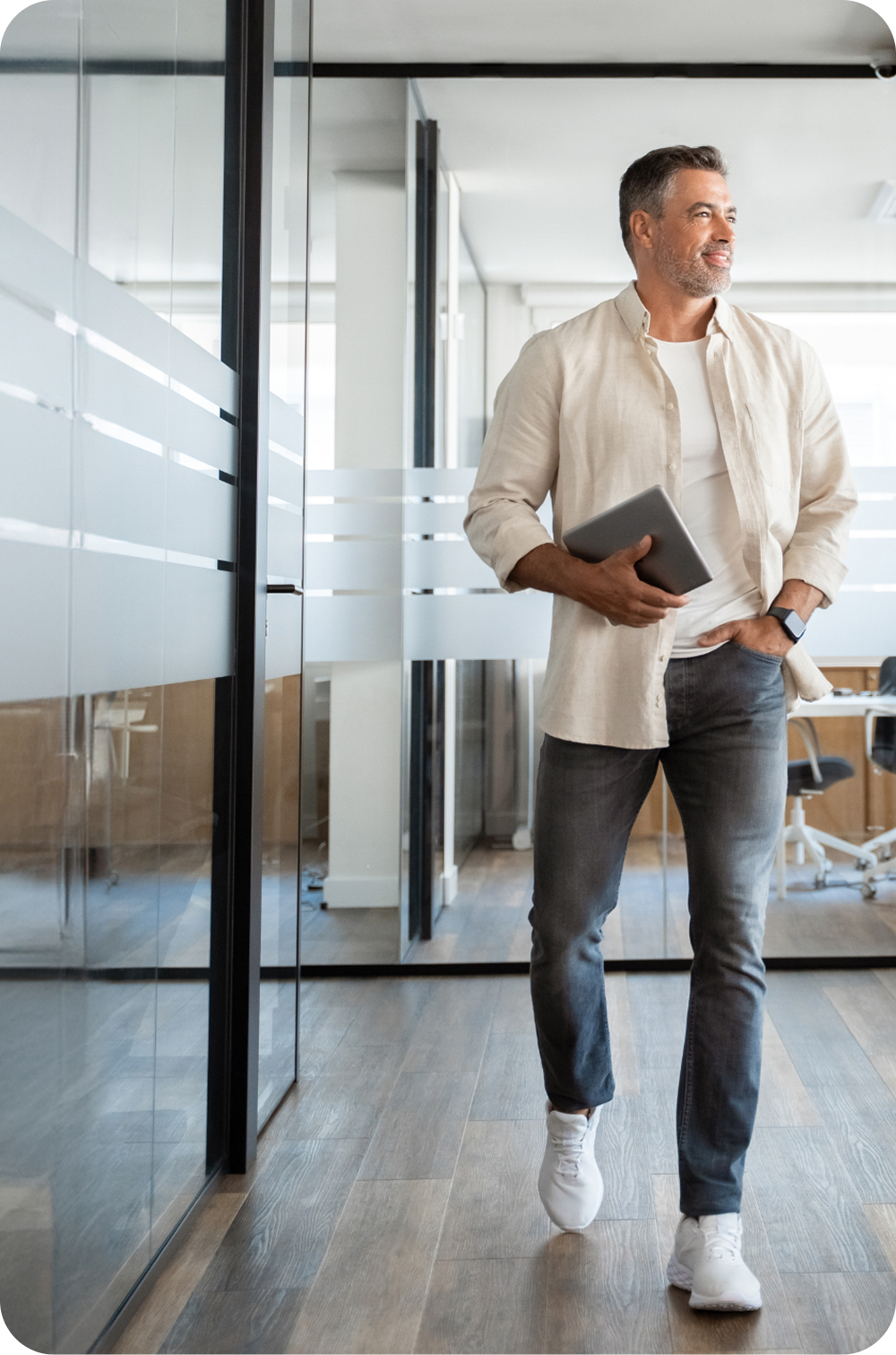 Man walking through a modern office hallway, holding a tablet and coffee cup