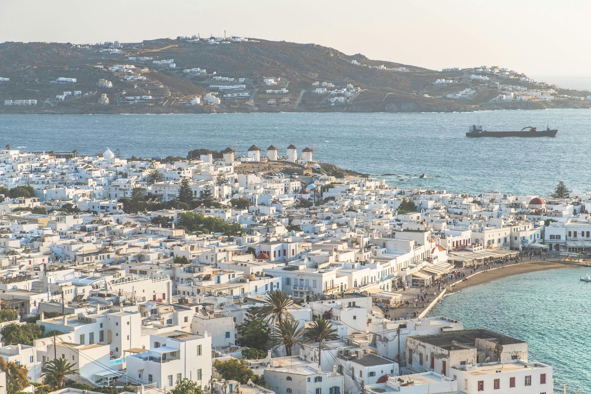 White coastal town with curved bay, blue water, and a ship on the horizon