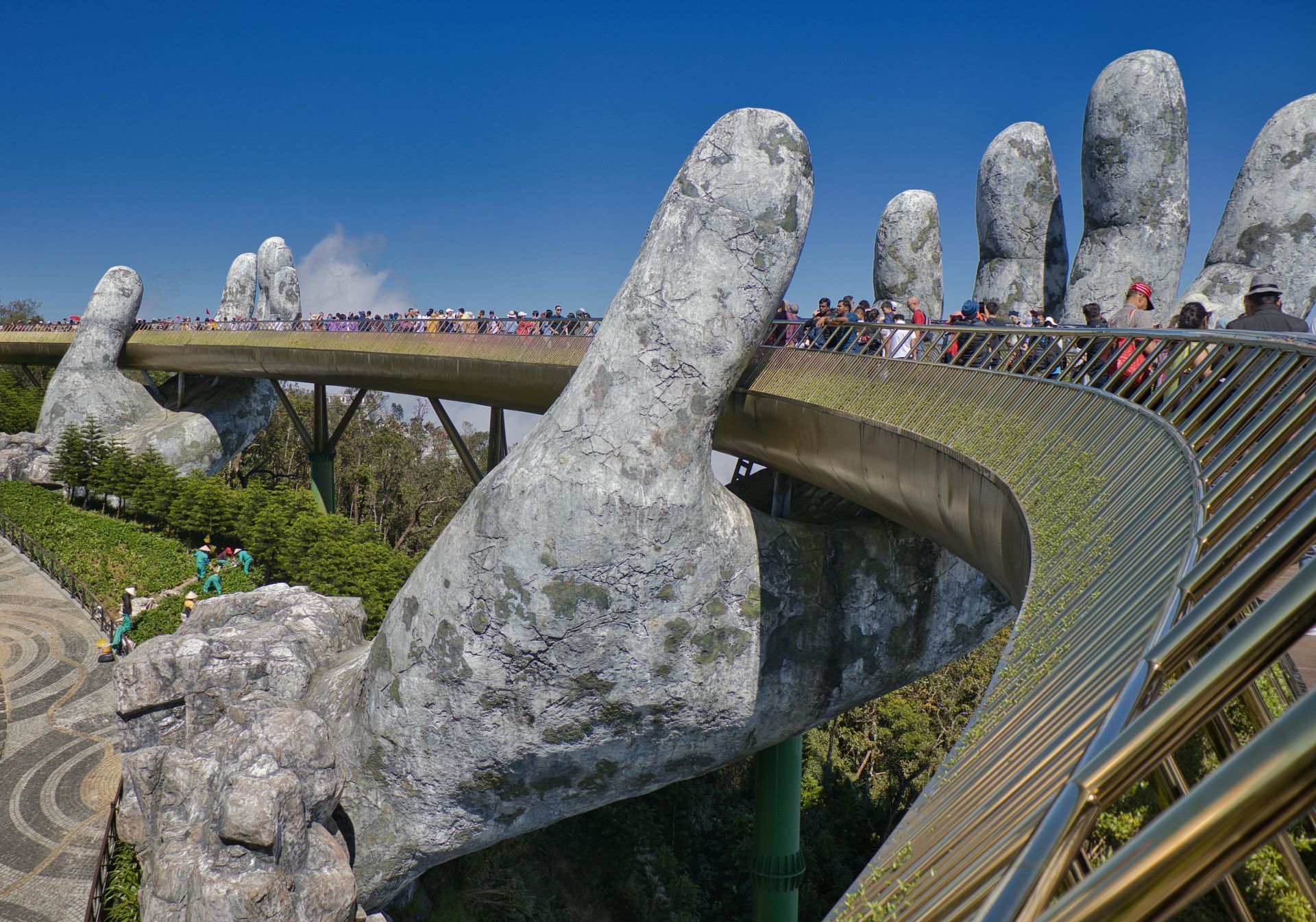 Golden Bridge with crowds walking beside giant stone hands under a clear blue sky