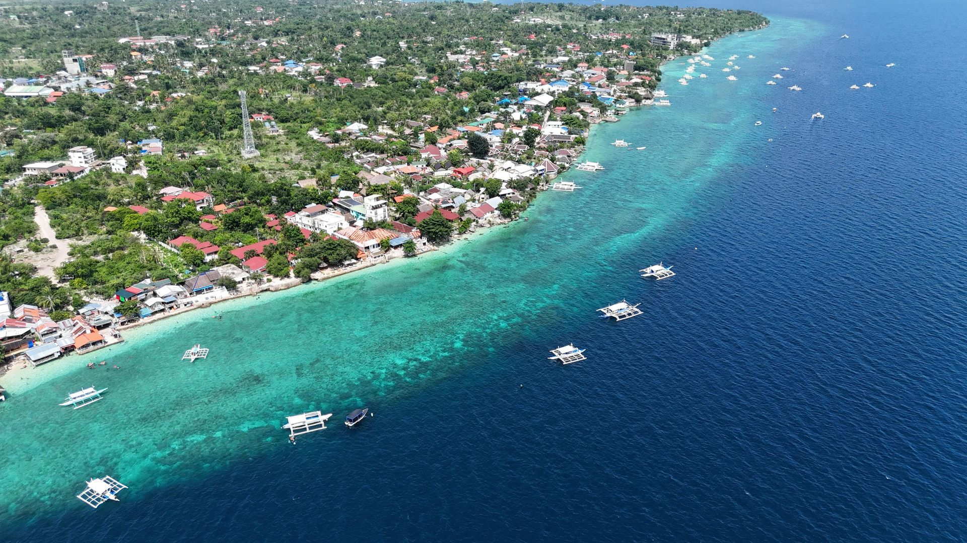 Aerial view of a coastal town with turquoise water, white boats, and a curved shoreline.