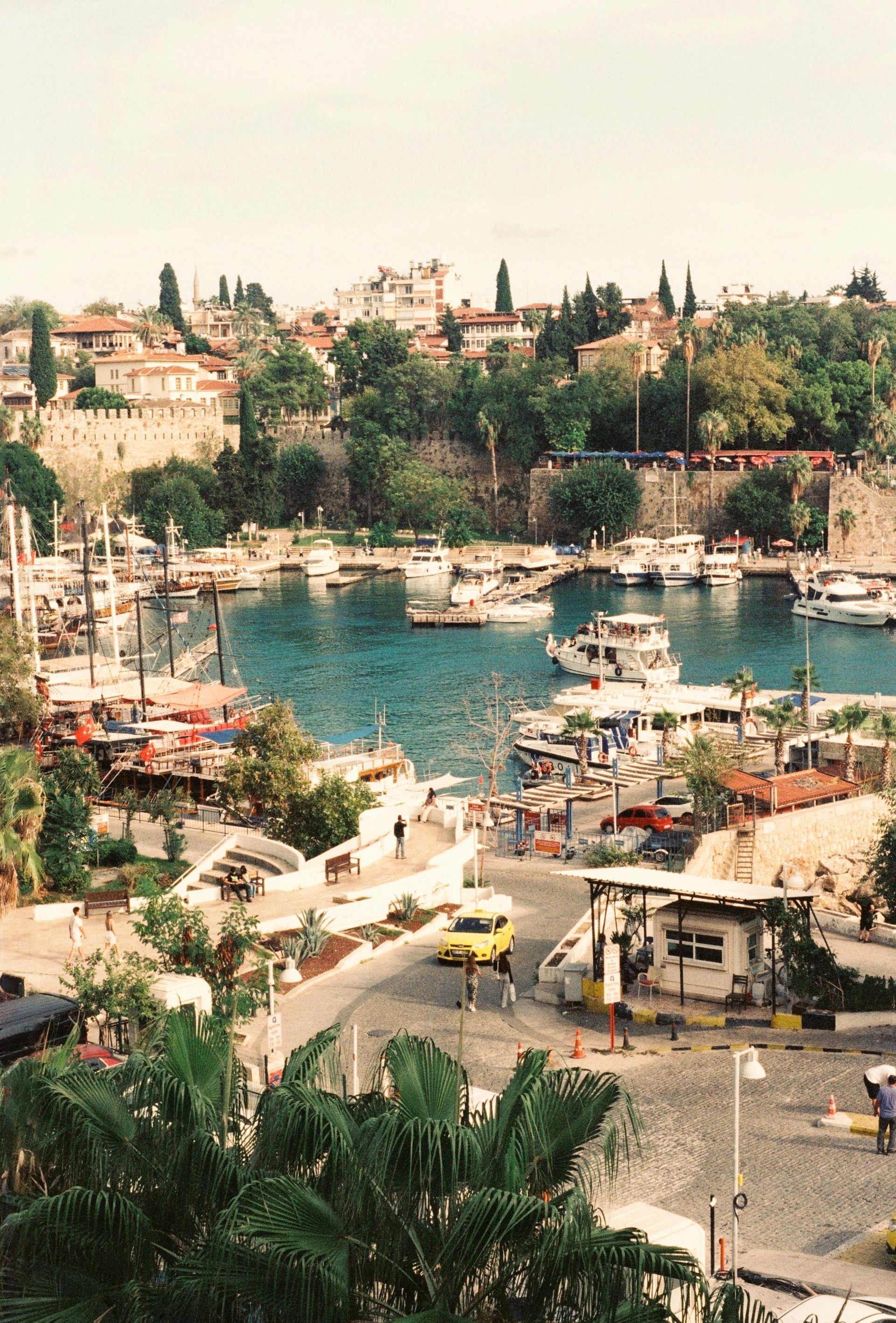 Harbor with boats and a turquoise bay, lined by trees and hillside buildings under a hazy sky