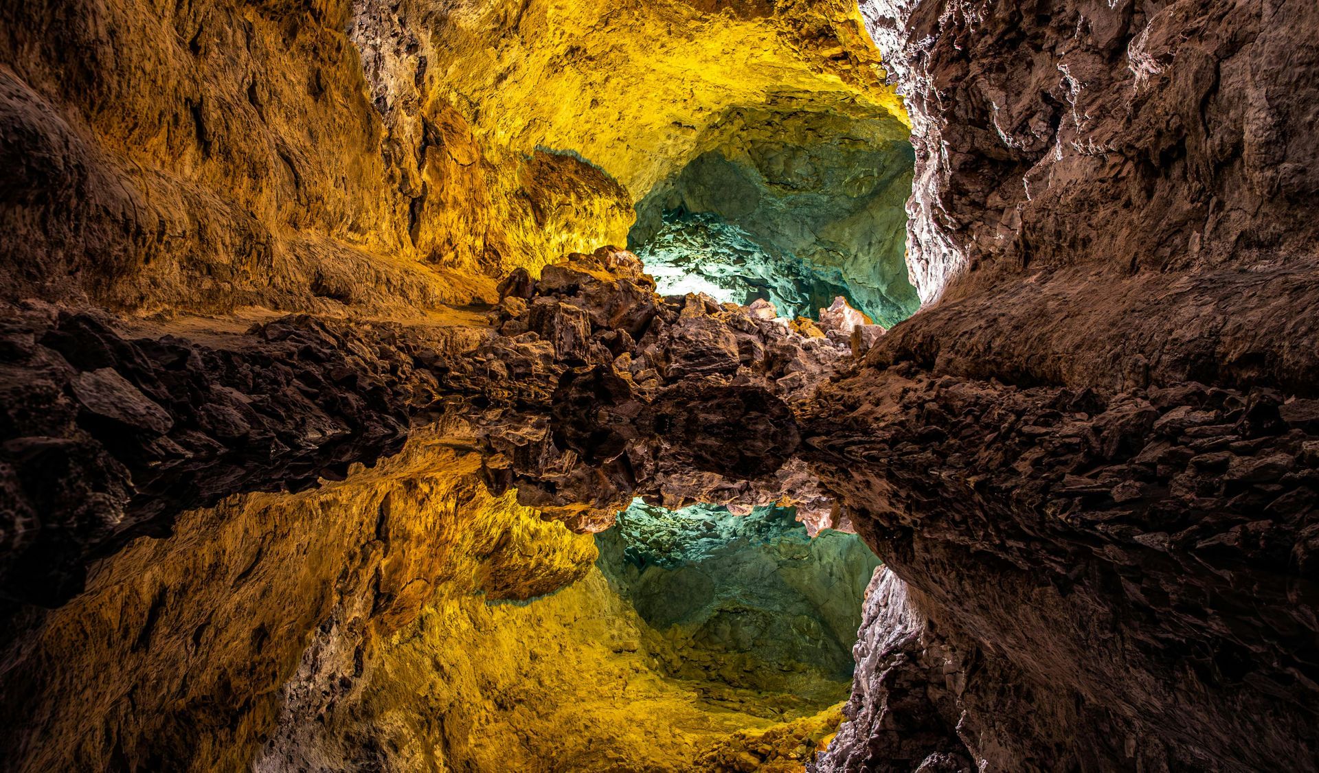 Reflective cave opening with yellow and brown rock framing a turquoise pool and sky above