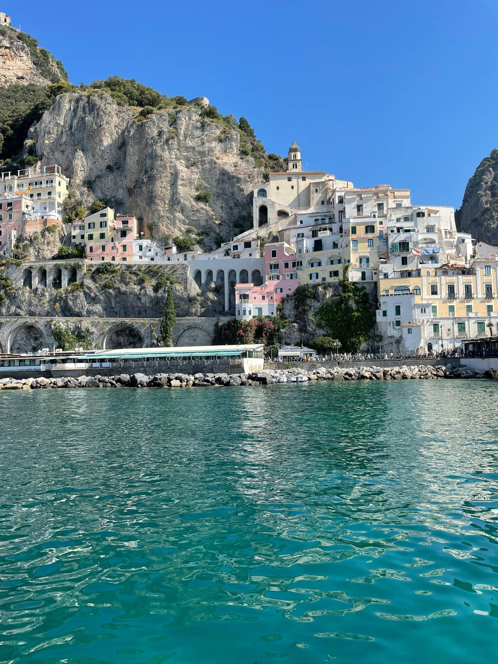 Colorful cliffside village above turquoise water under a clear blue sky.