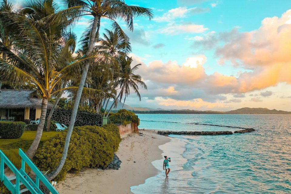 Tropical beach at sunset with palm trees, turquoise water, and a person walking along the shore