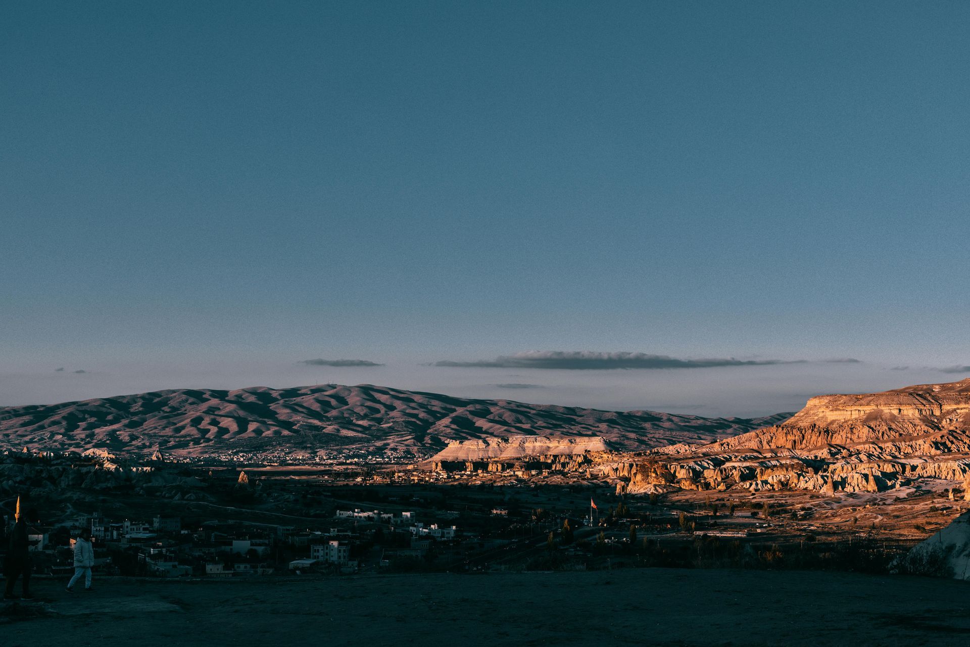 Wide cityscape at dusk with sunlit hillside homes under a clear blue sky