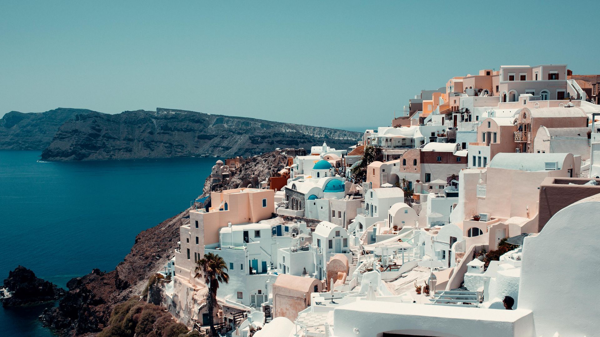 White seaside buildings on a cliff overlooking a blue sea and distant island, Santorini-style view